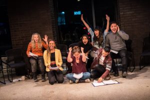 Cast of Towards Youth celebrating with their arms raised during a rehearsal