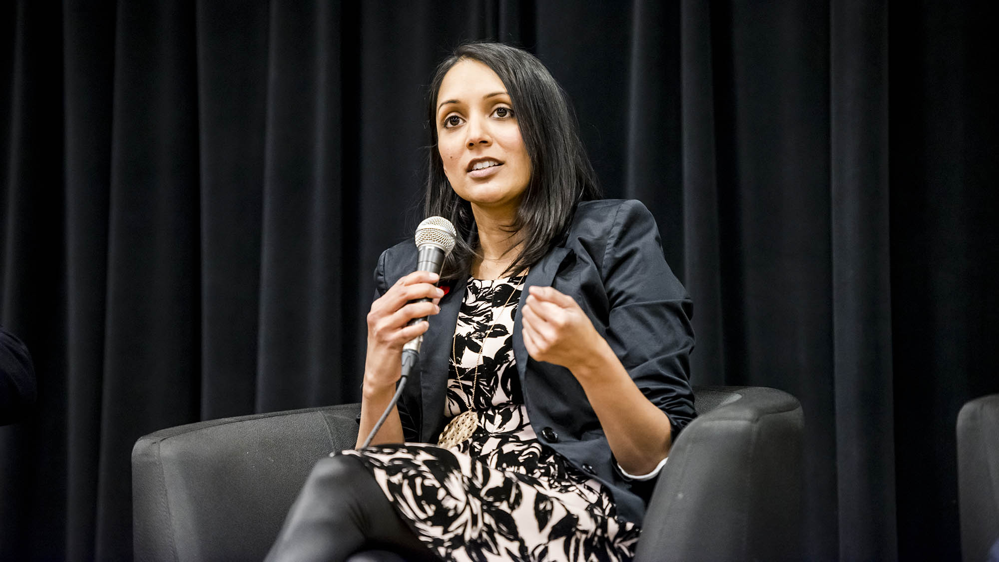 A person with a microphone delivering a speech while seated.