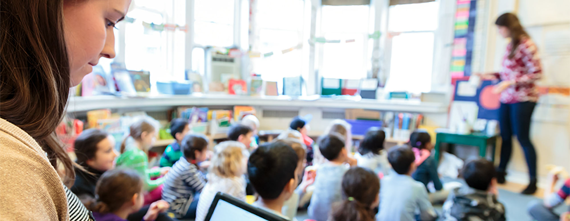 An educator teaching a variety of students in a classroom. Students are seated on a carpet.