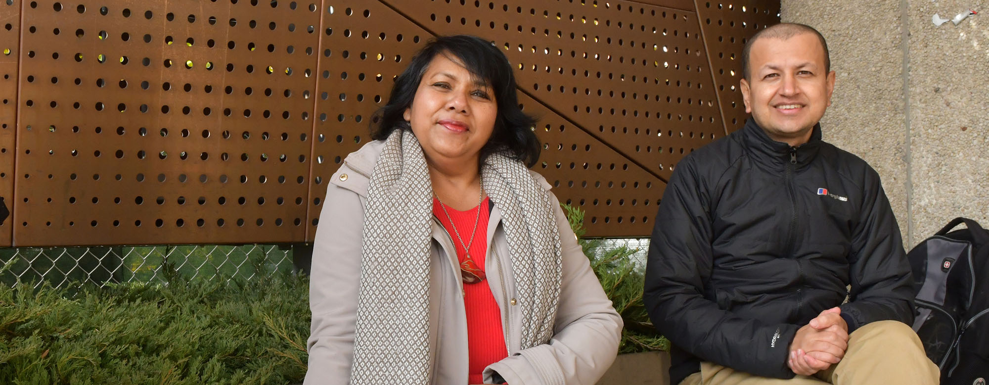 Two people sitting outside in front of the OISE sign.