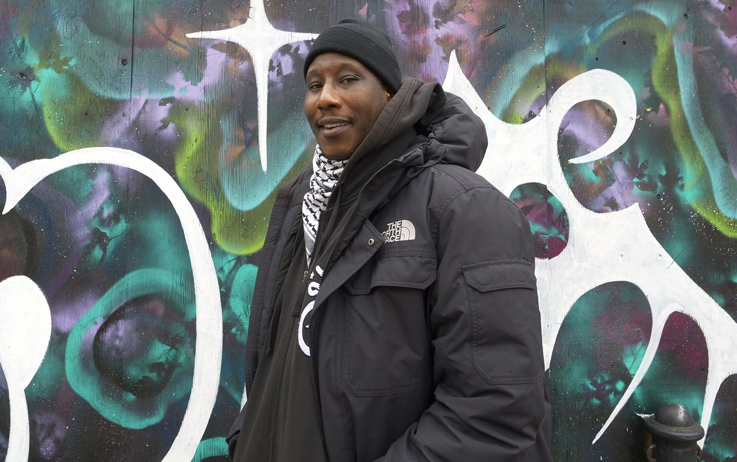 A student standing outside in a coat, with art in the background