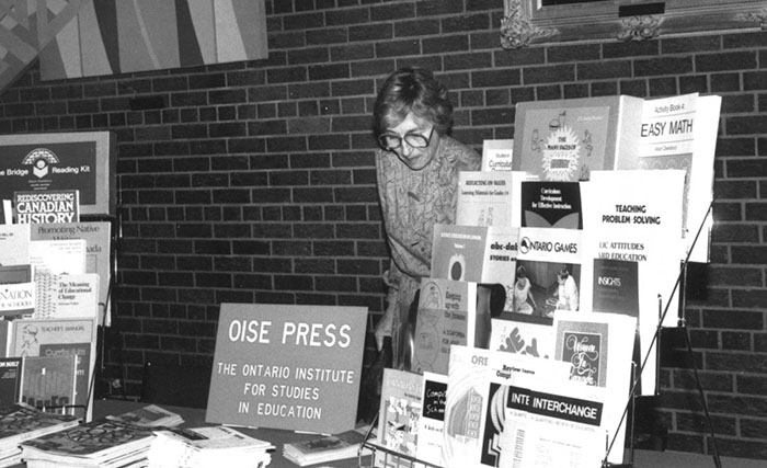 An individual standing by a table with OISE Press books and papers - Archive photo.