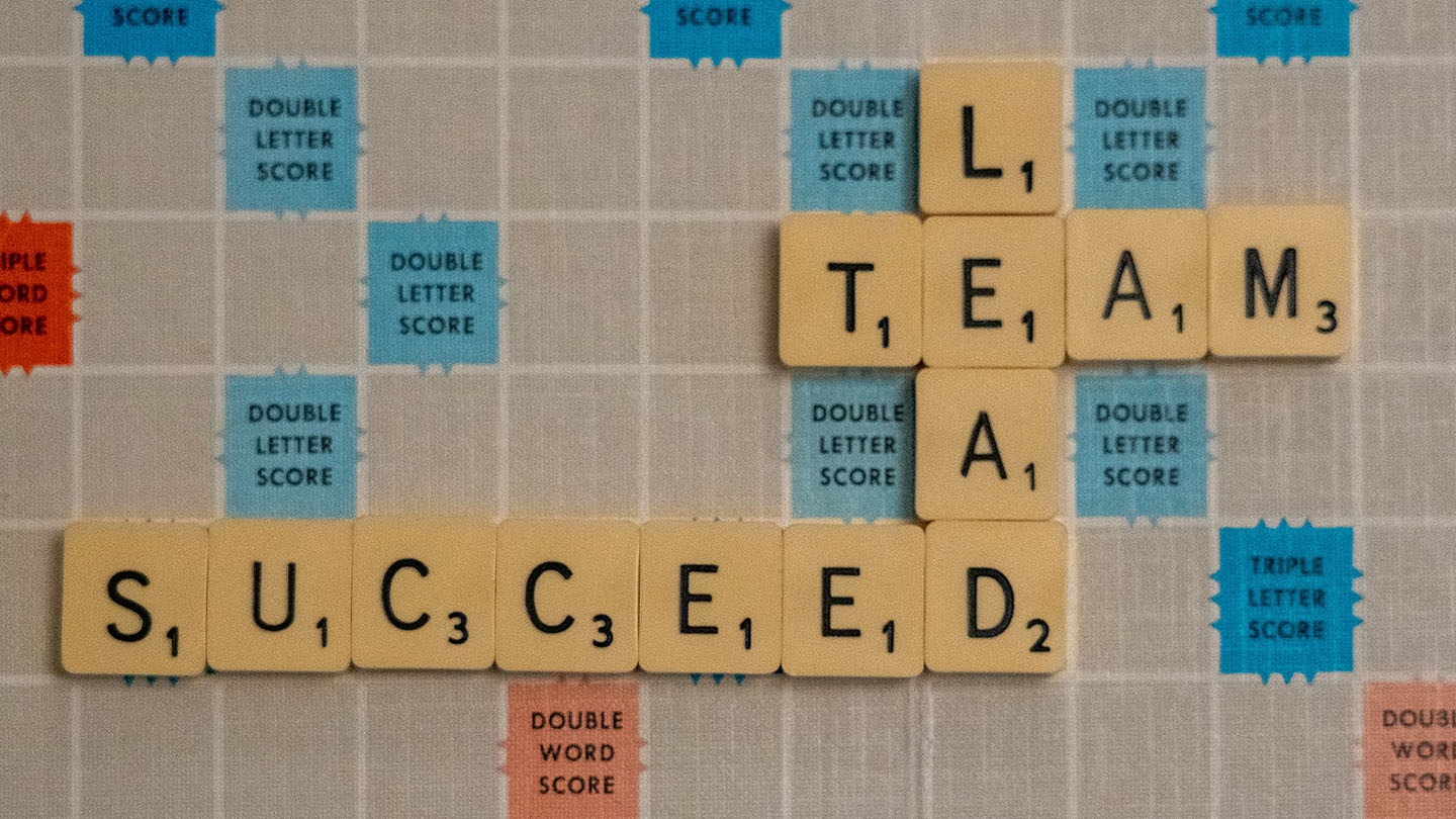 A Scrabble board with the connecting words: Lead, Team, and Succeed.