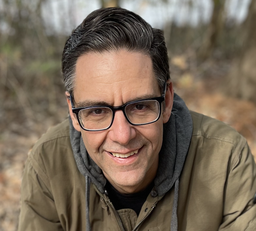 Man with short hair and glasses smiling outside