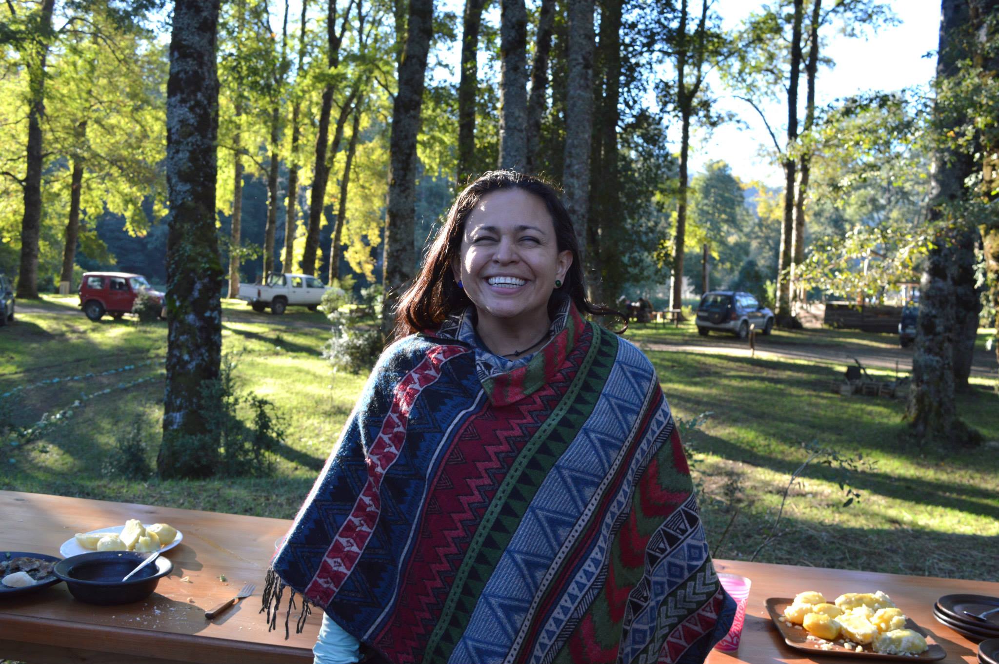 Woman smiling among trees, wearing a striped Pancho