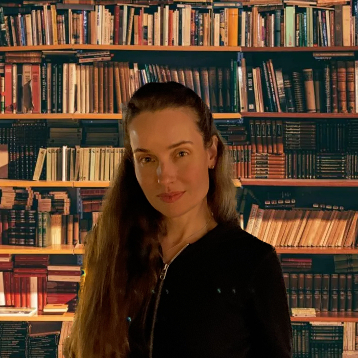 Woman with long hair, standing in front of a library bookshelf
