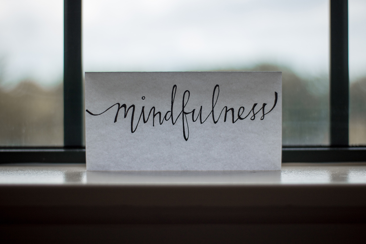 The word, mindfulness, written in cursive on a piece of paper by a in front of a window.