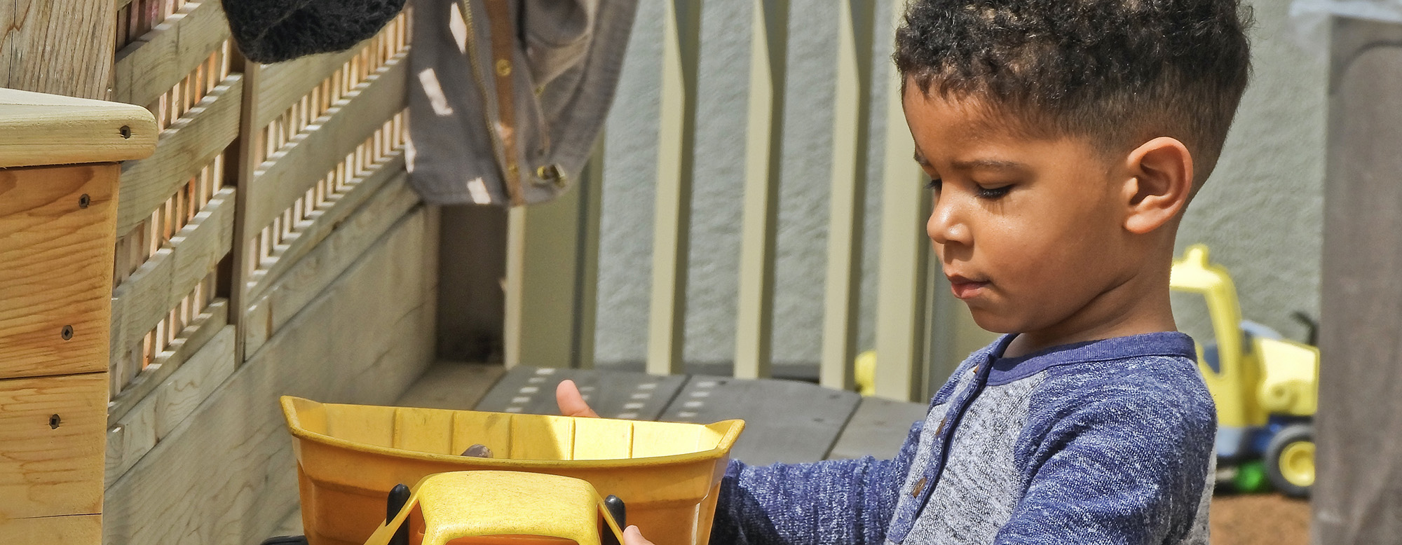 A child holding a yellow dump truck toy in a playground.