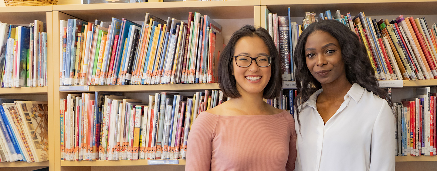 two adults standing in front of a bookcase in a classroom