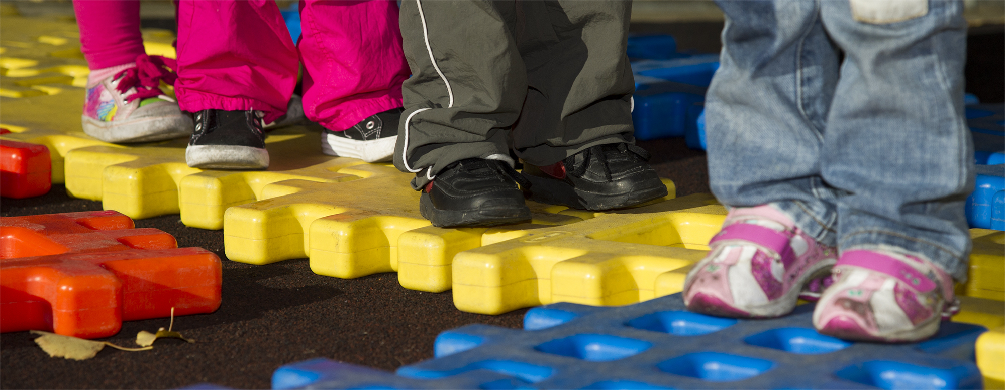 Four children playing on a playground puzzle. Only their shoes and the puzzle are visible.