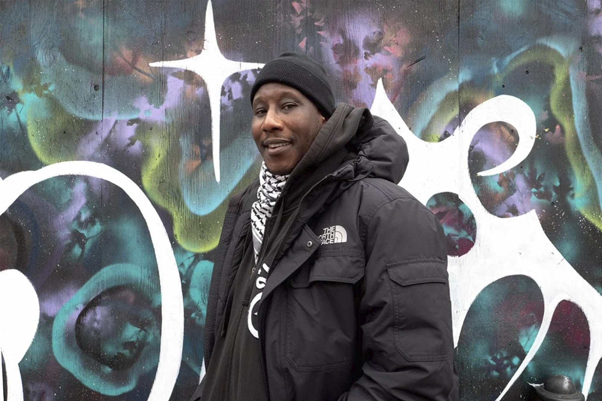 Marcus Singleton is smiling and standing in front of a graffiti mural