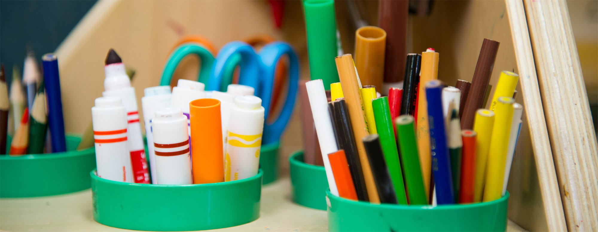 Markers, scissors, pencils, and pencil crayons in cups.