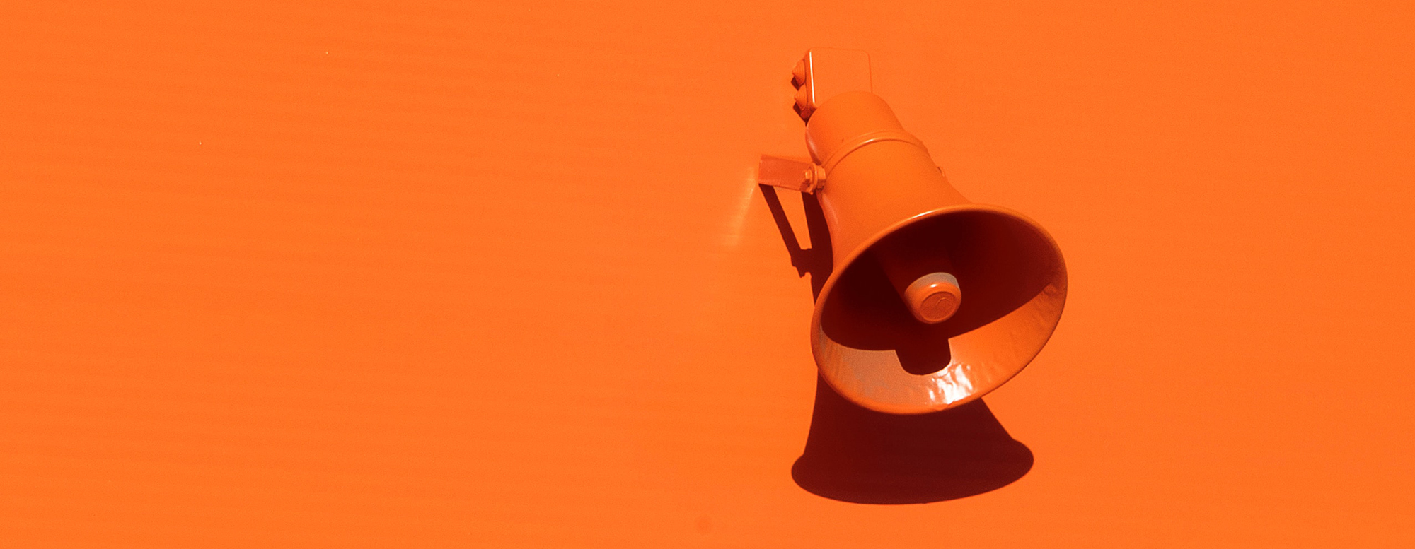 An orange outdoor speaker on an orange wall.