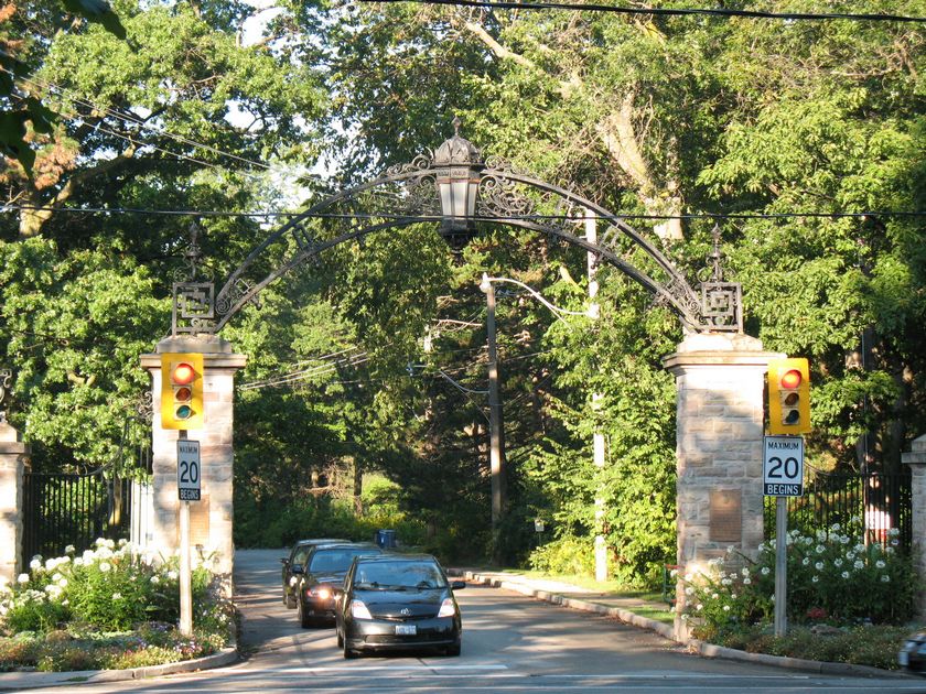 cars leaving through stone gate with trees in background