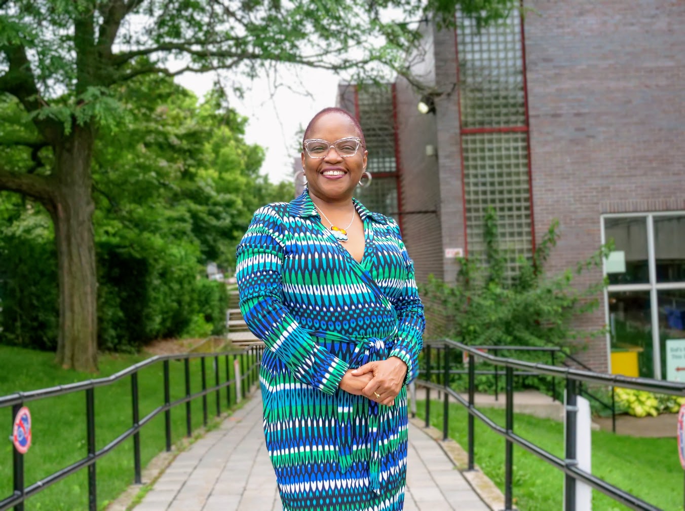 A Black woman is standing on an accessibility ramp with a big smile on her face