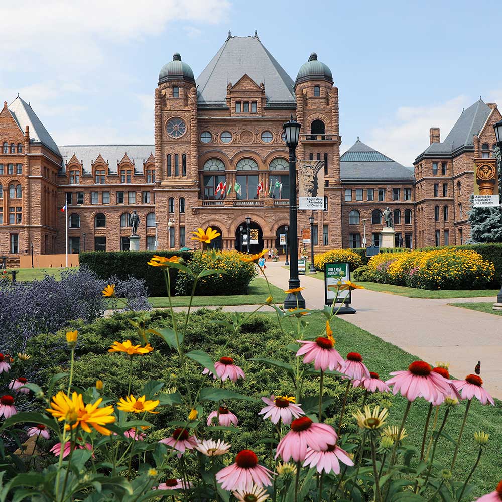 red stone building with copper roof against blue sky with gardens in front