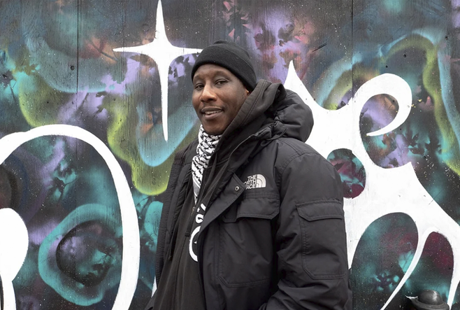 Marcus Singleton is smiling and standing in front of a graffiti mural