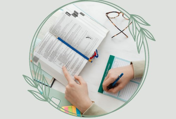 hands holding open a book and taking notes with spectacles on the side