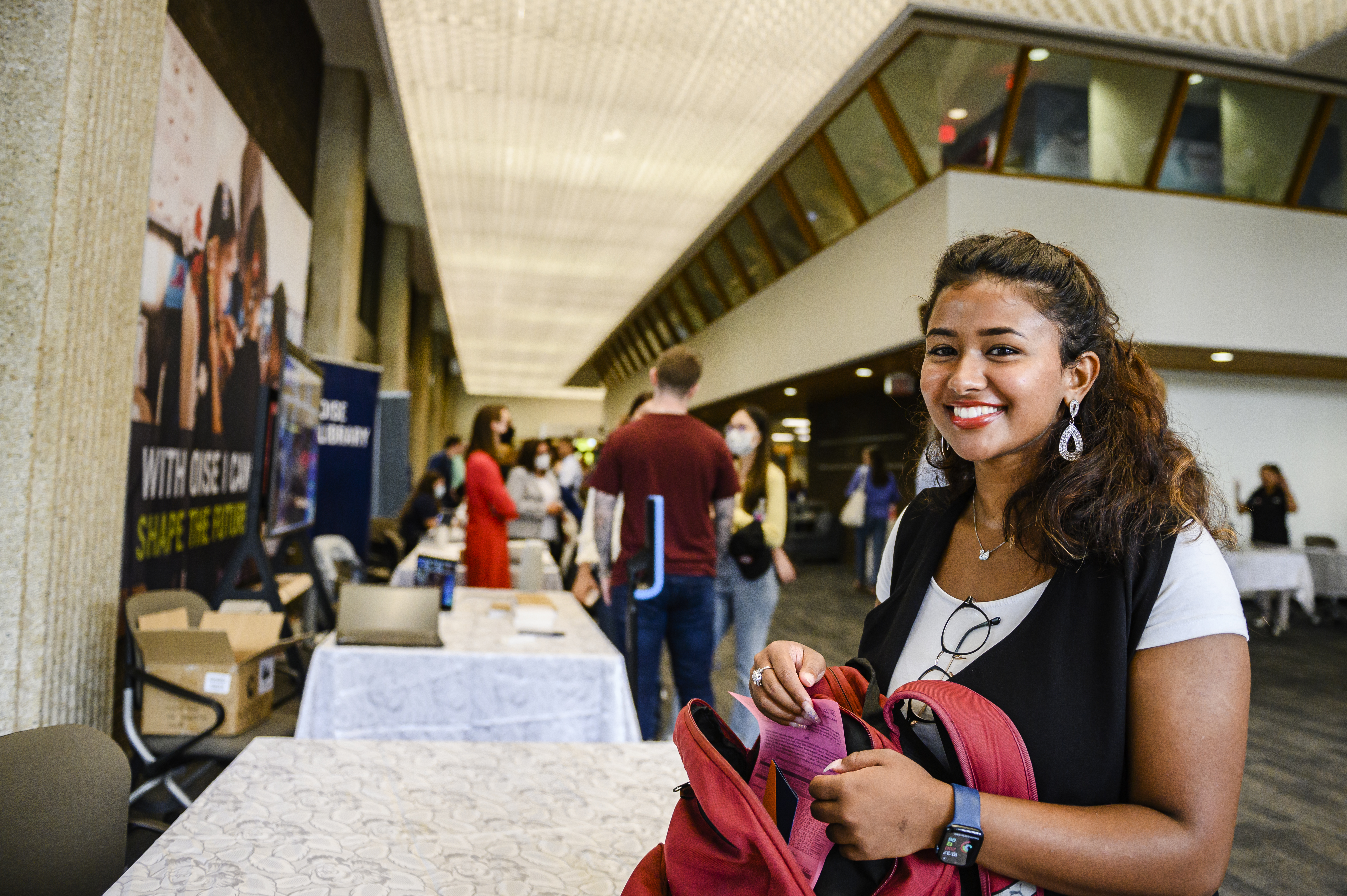 Young woman standing in the OISE library with her backpack and smiling at the camera.