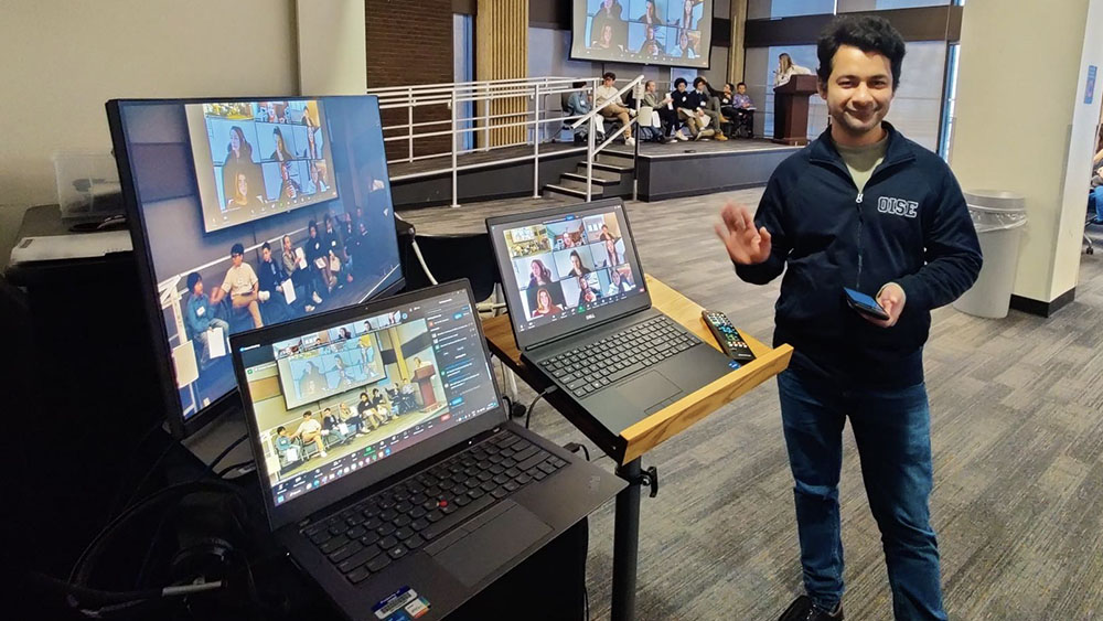 Education Commons team member, Azeem, standing beside two laptops and a monitor.