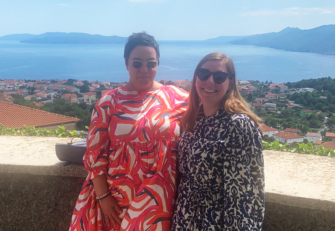 Professor Miglena Todorova and student Nana Gulic are standing next to each other and smiling, with Rijeka's coastline behind them.