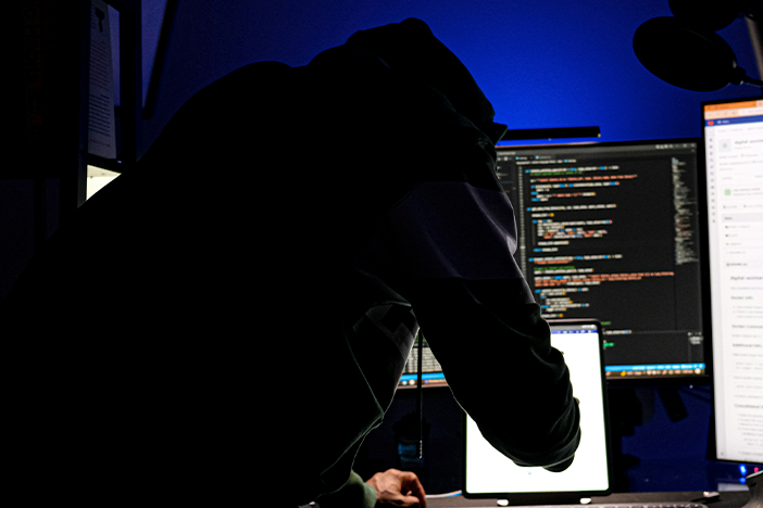 Person working at desk with multiple monitors displaying code in dimly lit room.