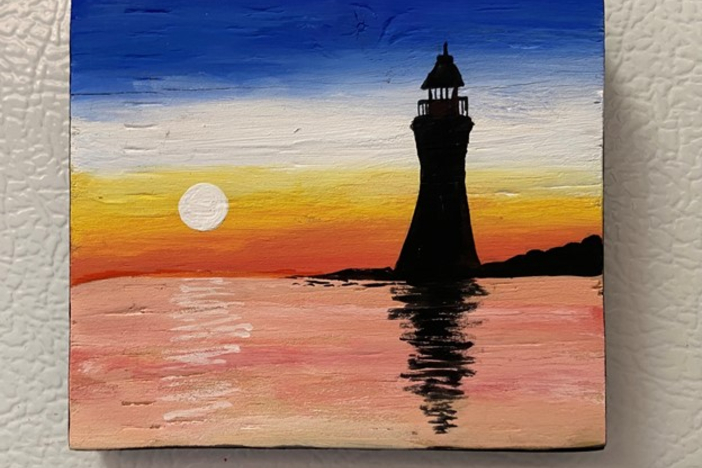 Silhouette image of a lighthouse reflected in water against the setting sun