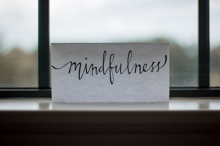 The word, mindfulness, written in cursive on a piece of paper by a in front of a window.