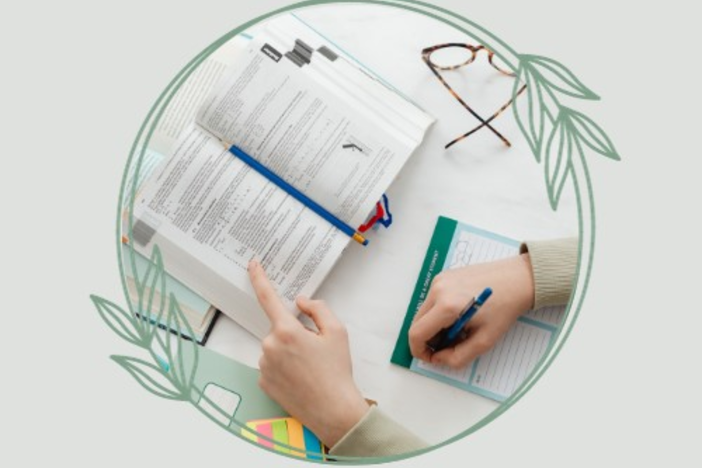hands holding open a book and taking notes with spectacles on the side