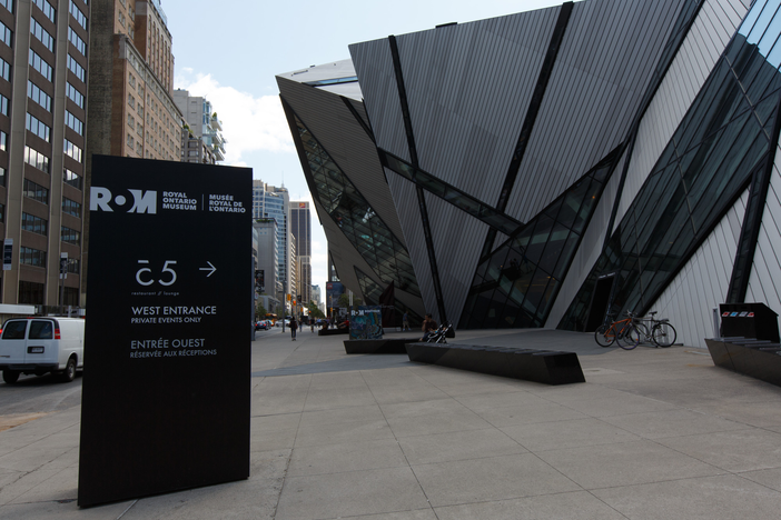 A brown sign post identifying a large angular glass and steel building as the Royal Ontario Museum