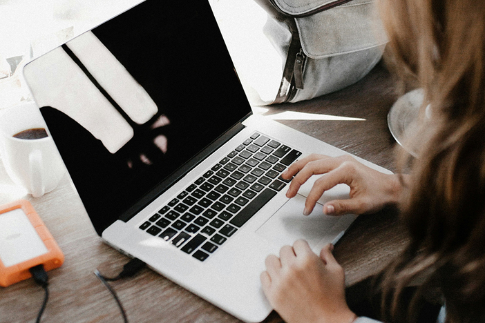 A person typing on a laptop, with a hard drive beside their device.