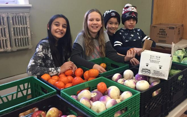 Four children in front of green bins of produce.