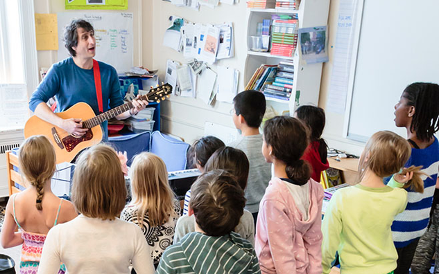 Students listening to a teacher playing a guitar.