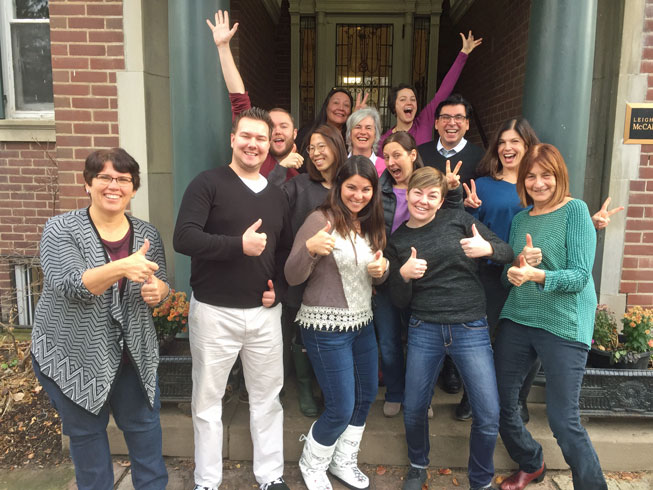 A group of people posing happily outside a building, many giving thumbs up.