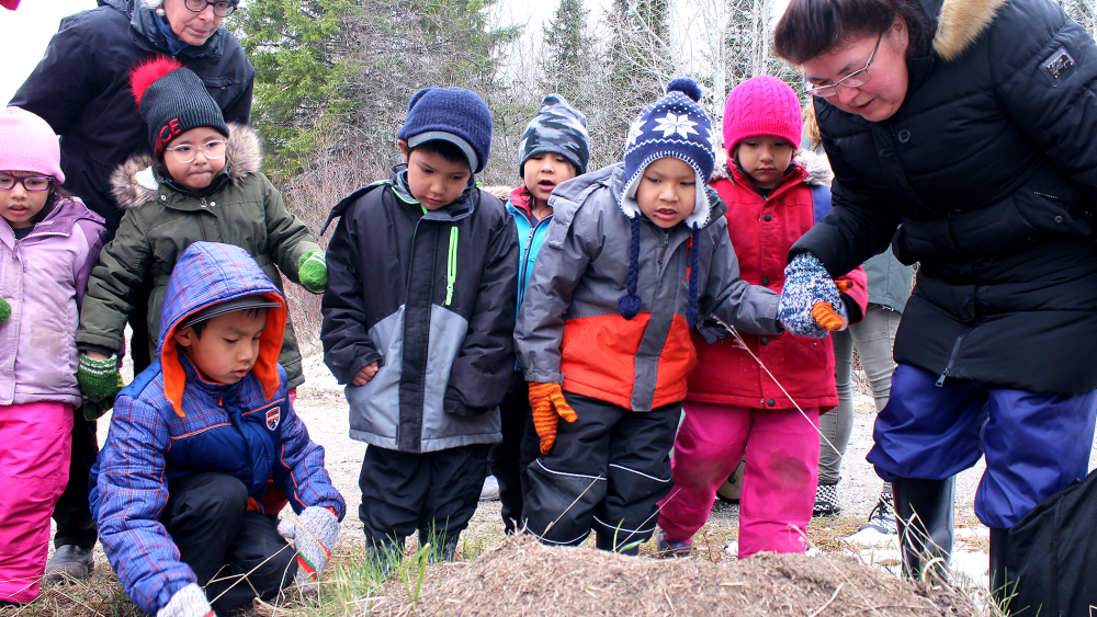 A group of children dressed in winter clothing, gathered around an adult who is also dressed in winter attire.