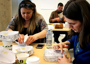 A group of people sitting at a table, engaged in an activity involving paper or cardboard objects.