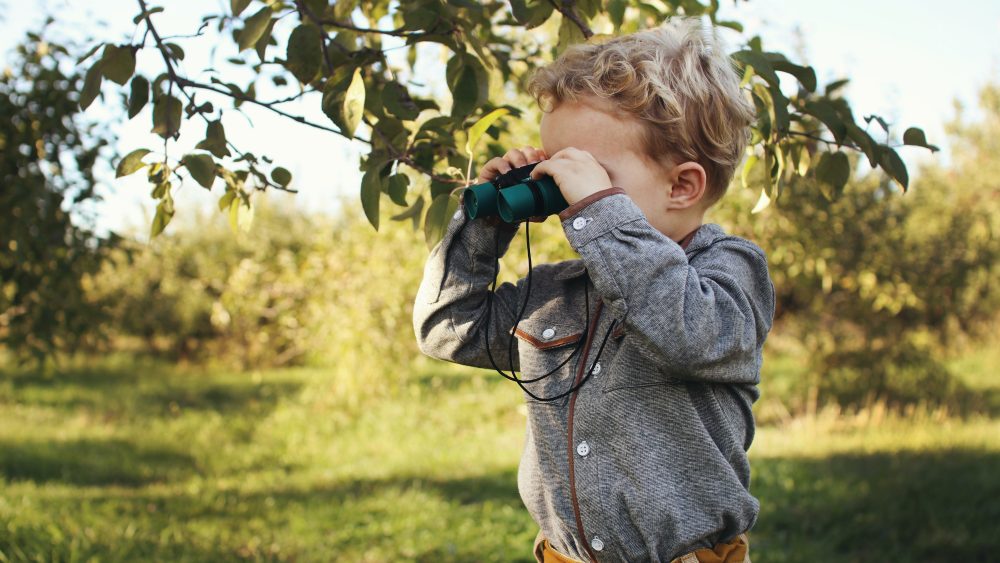 A child looking through a a set of binoculars outside.