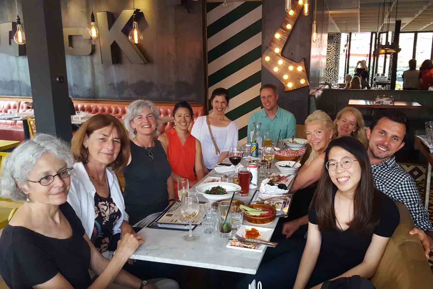 A group of people sitting around a table in a restaurant with plates of food and drinks.