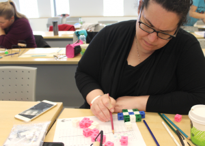 A person sitting at a desk working with pink and multicolored cubes, writing on graph paper.