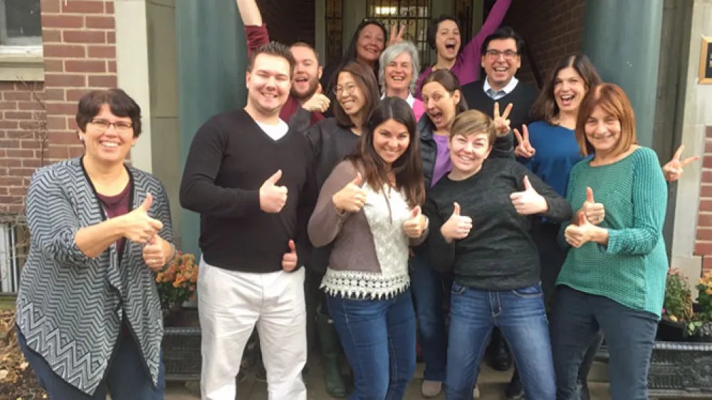 A group of people posing happily outside a building, many giving thumbs up.