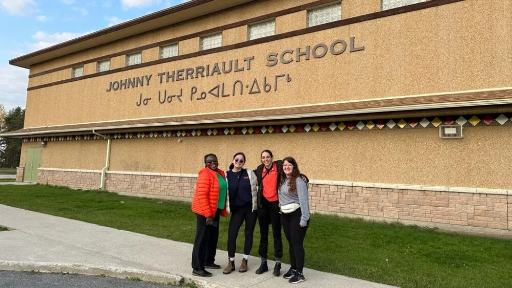 Four people standing in front of Johnny Therriault School.