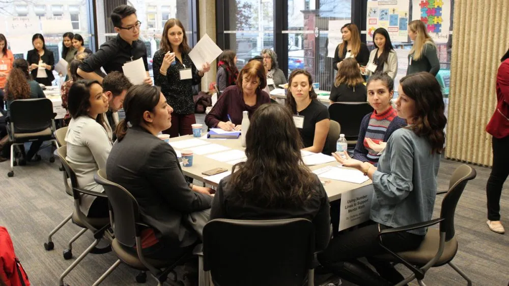 A group of people sit and stand around tables engaged in a collaborative workshop or discussion.