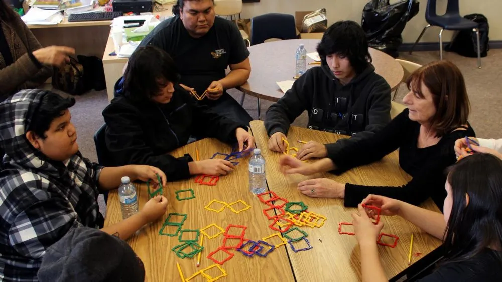 A group of people sitting around a table, engaging in an activity involving colorful geometric shapes made from sticks and connectors.