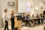 A panel of speakers seated at a long table with two women standing at a podium, presenting on global climate education. A screen behind them displays the presentation title.