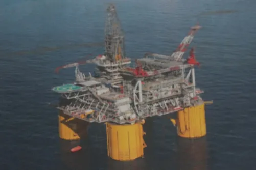 Offshore oil platform with large yellow legs and a complex structure on top, situated in a calm sea.