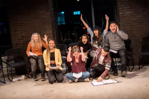 Cast of Towards Youth celebrating with their arms raised during a rehearsal