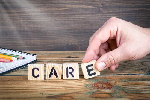 The word 'care' spelled with letters on wood blocks with a hand holding the letter 'E'