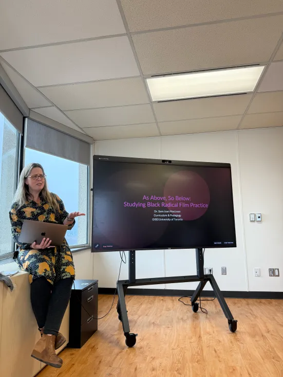 A person presenting beside a tv screen