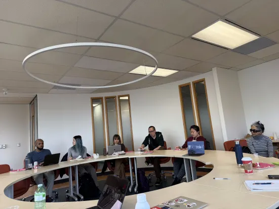 A group of people having a discussion, seated around a round table.