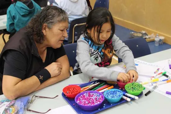 A woman and a young girl sit at a table sorting colorful beads.